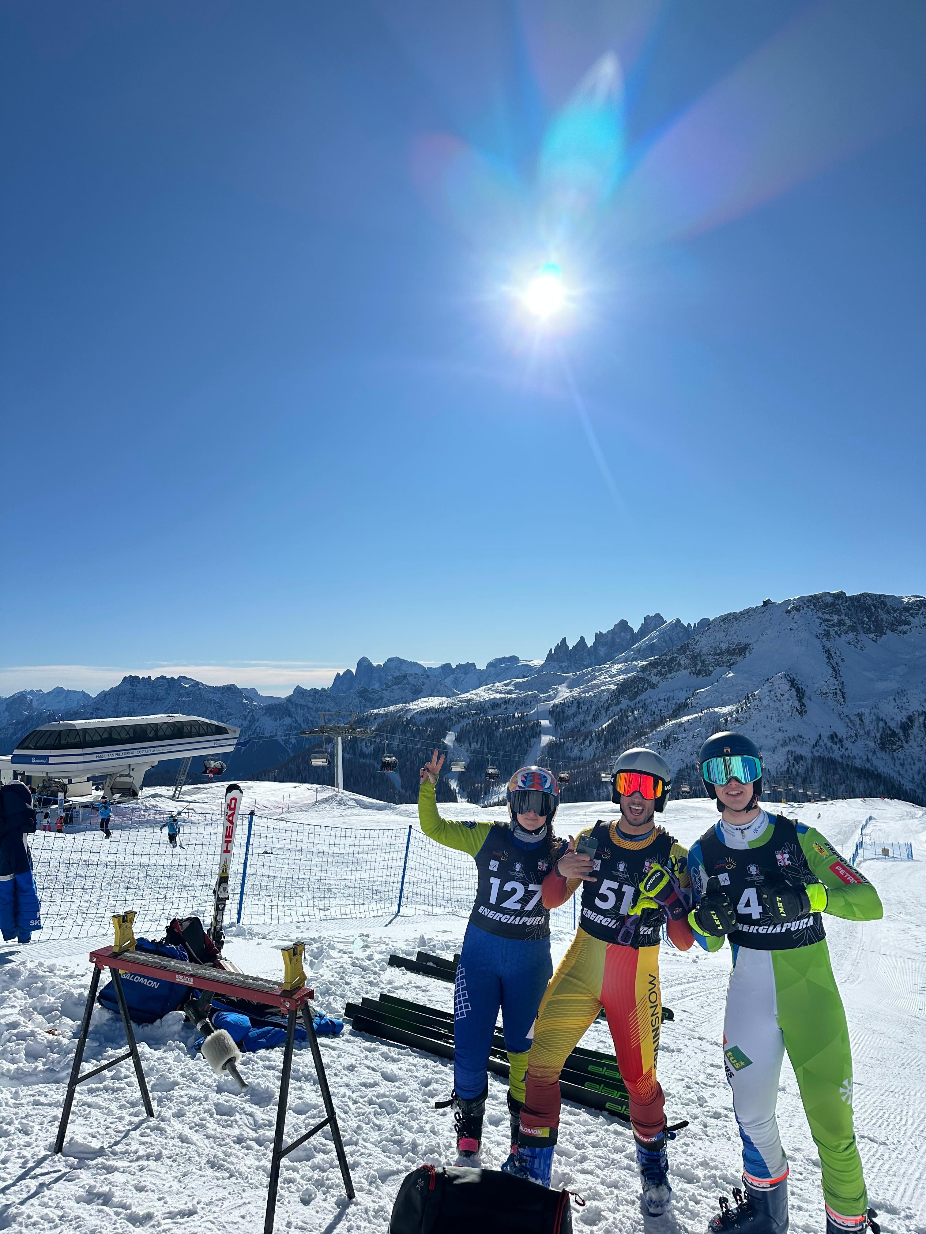Tres corredores con dorsal sonríen en la zona de salida, con montañas nevadas al fondo.