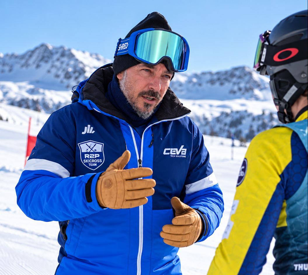 El entrenador Héctor Júlvez habla con una deportista en la pista, con montañas nevadas al fondo.