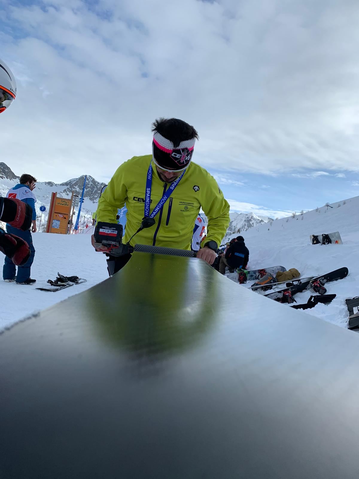 Un técnico repasa la suela de un esquí con una herramienta eléctrica, a pie de pista.