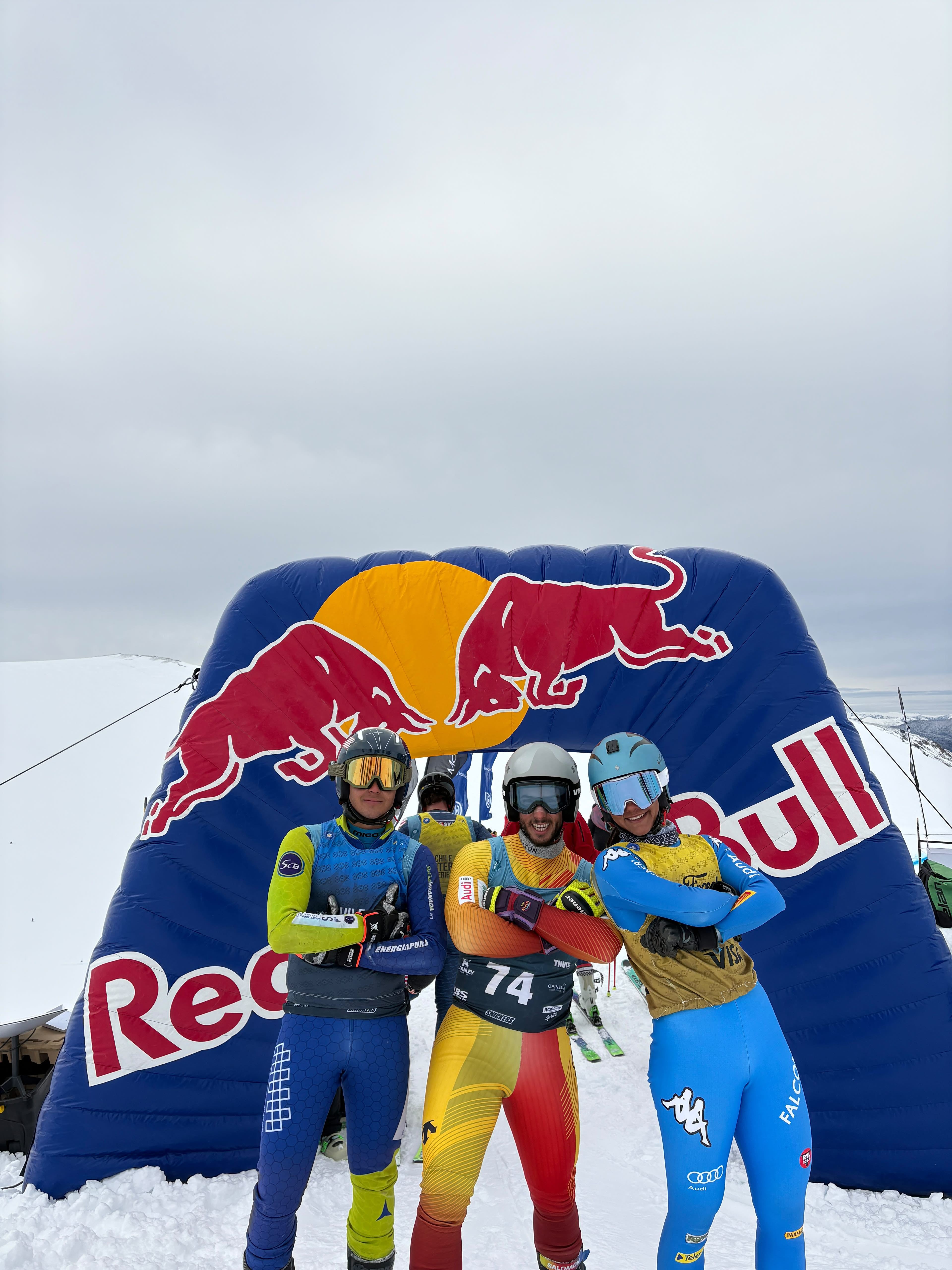 Tres corredores de skicross posan con los brazos cruzados bajo el arco hinchable de meta, en la nieve.