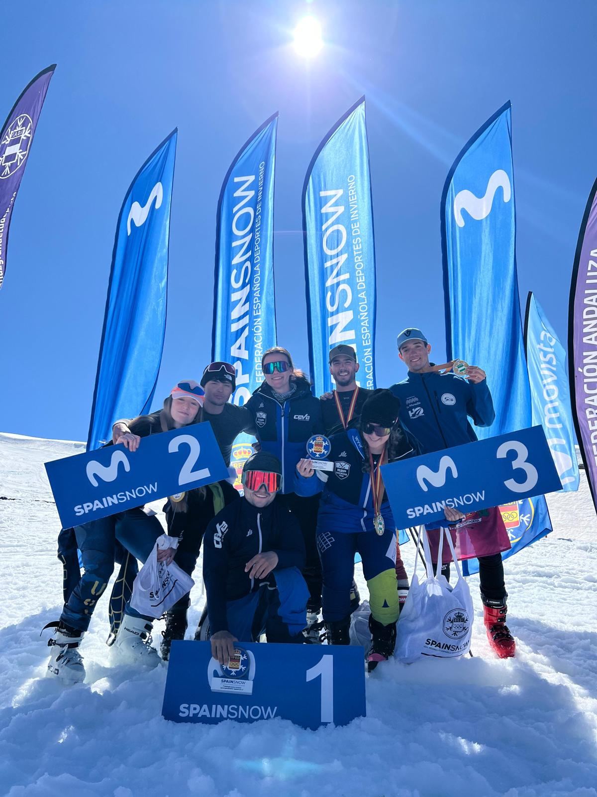 Corredores del equipo celebran un podio en la nieve, con medallas y trofeo.