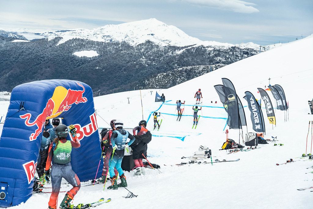 Corredores en la zona de salida y una manga en el circuito, con montañas nevadas al fondo.